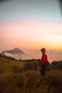 Rear view of man on field against sky during sunset