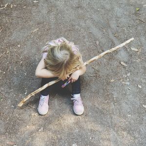 High angle view of tired girl sitting with stick on dirt road
