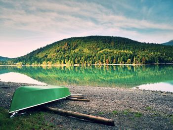 Abandoned fishing paddle boat on bank of alps lake. morning lake glowing by sunlight.