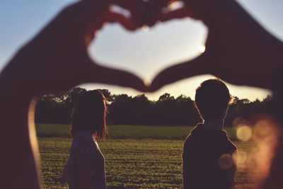 Rear view of mother with heart shape against sky during sunset