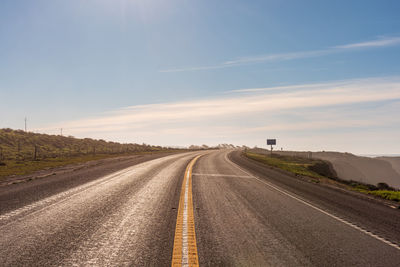 Road passing through field against sky