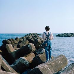 Man standing on rock by sea against sky