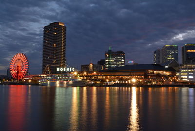 Illuminated buildings by river against sky at night