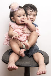 Cute siblings sitting on stool against white wall