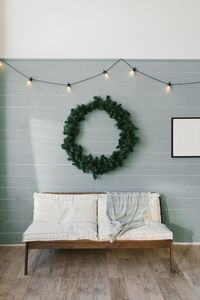 Wooden sofa with white soft pillows and a large christmas wreath on the wall, lined with clapboard