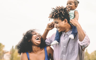 Cheerful family laughing while standing outdoors against sky