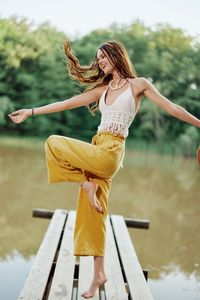 Side view of young woman with arms raised standing against trees