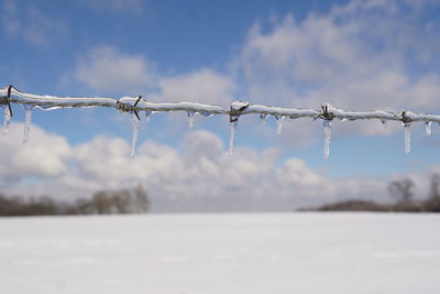Close-up of barbed wire fence against sky during winter
