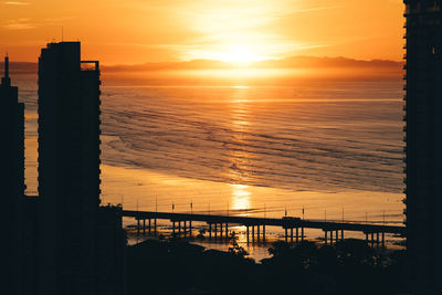 Silhouette building by sea against orange sky