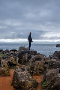 Rear view of man standing on rock at beach against sky