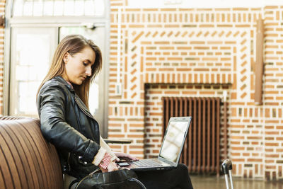 Side view of businesswoman with laptop sitting at waiting area in railway station