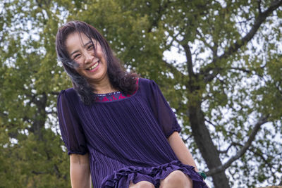 Portrait of smiling senior woman against tree outdoors