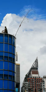 Low angle view of crane by building against sky