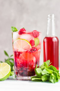 Cold pink non-alcohol cocktail with raspberry, lime, mint and ice cubes on light grey background.