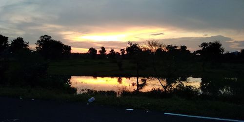 Silhouette trees by lake against sky during sunset