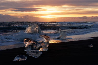 Snow covered land by sea against sky during sunset