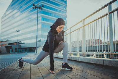 Beautiful woman wearing hijab exercising against building during sunrise