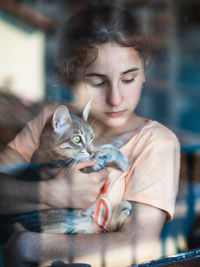 Portrait of young woman through a window holding a cat.