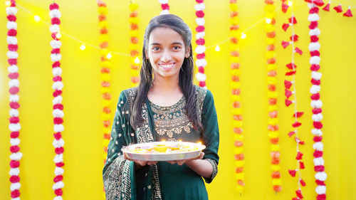 Young girl holding diwali oil diya on her hand in fairy light background and smiling from the heart.