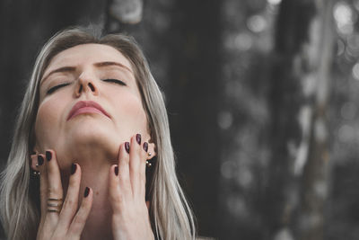 Woman with closed eyes touching neck outdoors