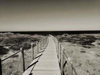 Pier leading towards sea against clear sky