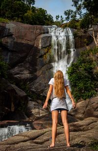Rear view of woman standing on rock against waterfall