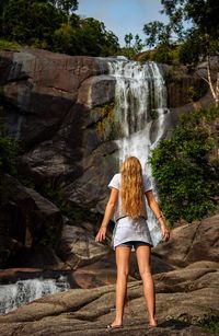 Rear view of teenage girl standing against waterfall