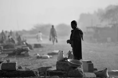 Side view of man standing by rocks on field against sky