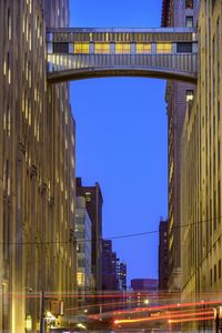 Low angle view of illuminated bridge against buildings at dusk