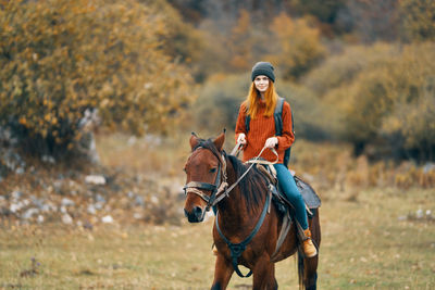 Full length of young woman riding horse on field