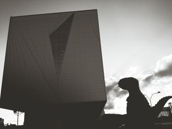 Low angle view of silhouette woman standing against sky in city