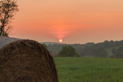 Close-up of hay bales on field against sky during sunset