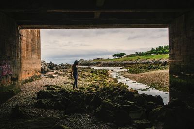 Woman standing on rock by sea against sky