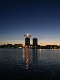 Illuminated lighthouse by sea against clear sky