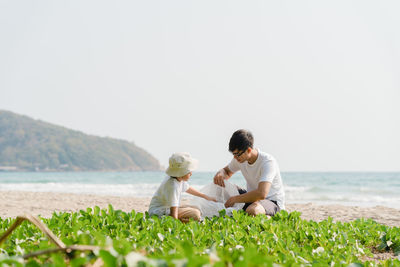 Friends sitting on grass by sea against sky