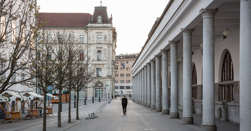 Rear view of person walking on street amidst buildings in city