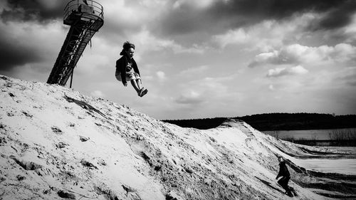 A boy is jumping from a sand dune against sky
