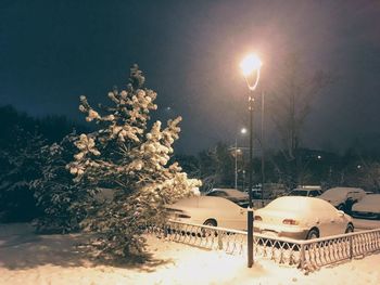 Snow covered street by trees against sky at night