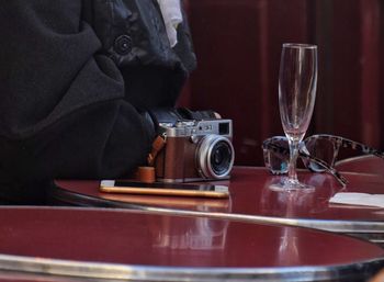 Midsection of person sitting by table with camera and smart phone