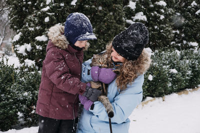 Portrait of happy family mother, son and cat in snowy winter park. outdoors portrait of mom and kid