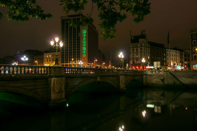 Illuminated bridge over river by buildings in city at night