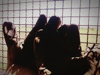 Close-up of silhouette hand by chainlink fence against sky