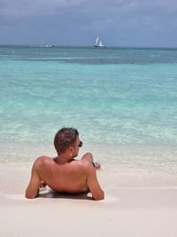 Man sitting on beach by sea against sky