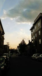 Cars parked on road by buildings against sky during sunset