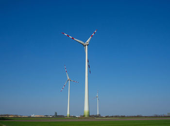 Low angle view of wind turbines on field against clear blue sky