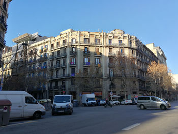 Cars on road by buildings against clear blue sky