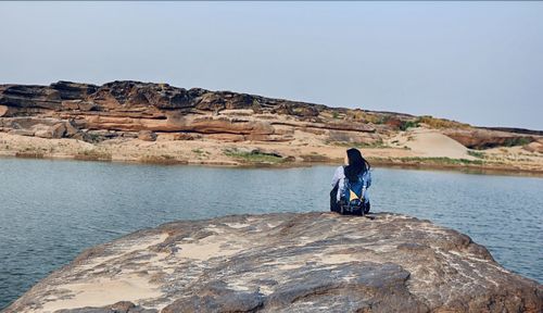 Rear view of woman sitting on rock against sky