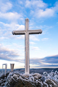 Cross on snow covered land against sky