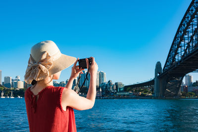 Rear view of woman photographing sydney harbor bridge against clear sky