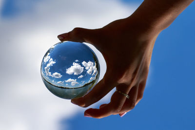 Cropped image of woman holding crystal ball against blue sky